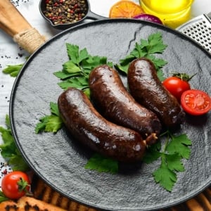 Finished blood sausage recipe on a plate with tomatoes and parsley.