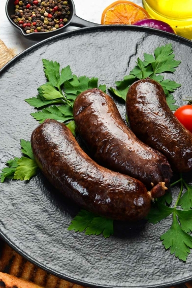 Finished blood sausage recipe on a plate with tomatoes and parsley.
