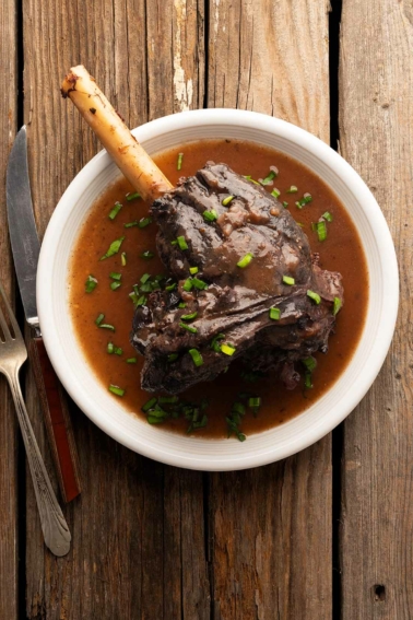 A braised deer shank on a plate with sauce, ready to eat.