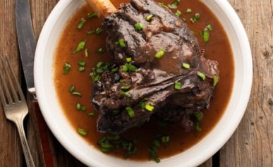A braised deer shank on a plate with sauce, ready to eat.