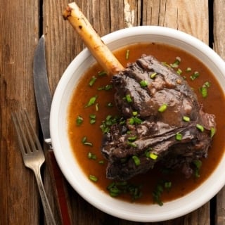 Close up of a braised deer shank with a brown sauce on a plate.