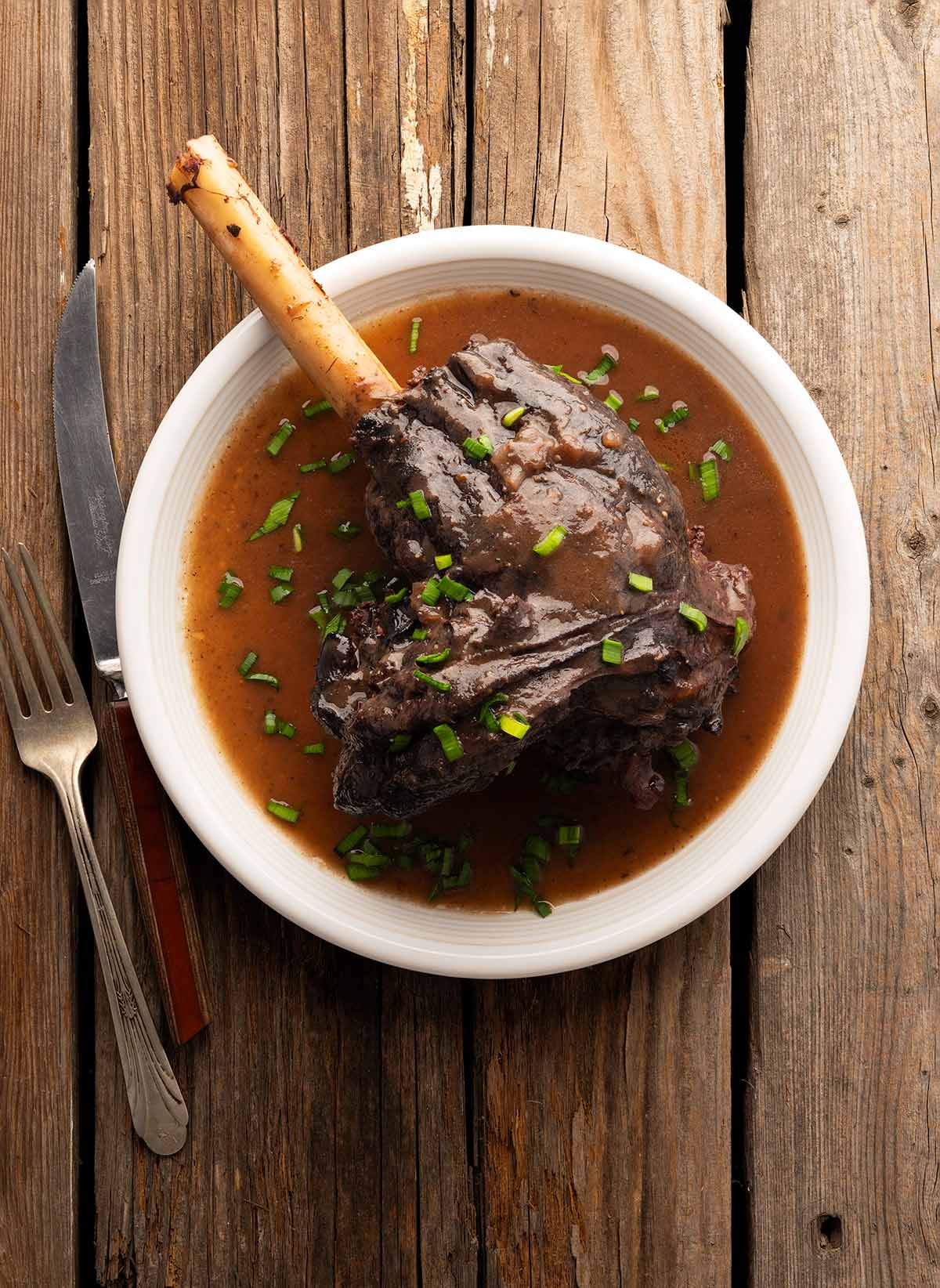A braised deer shank on a plate with sauce, ready to eat. 