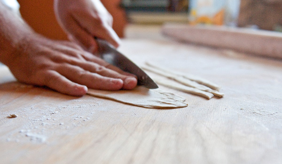 Slicing lengths of dough for pici pasta. 