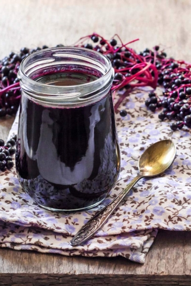 Elderberry syrup in a jar, surrounded by ripe elderberries.