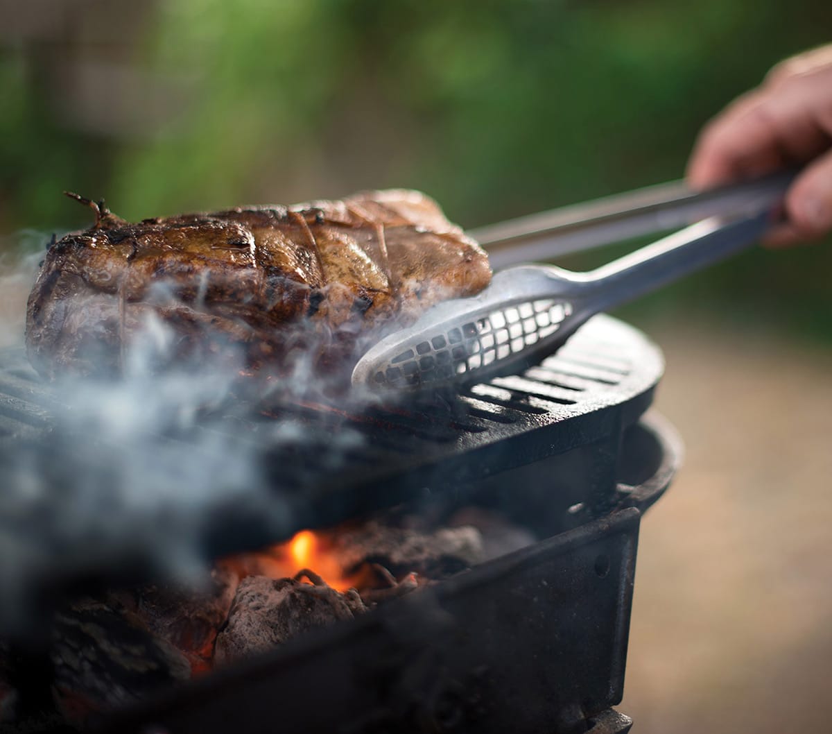 Flipping grilled venison steak over the fire. 