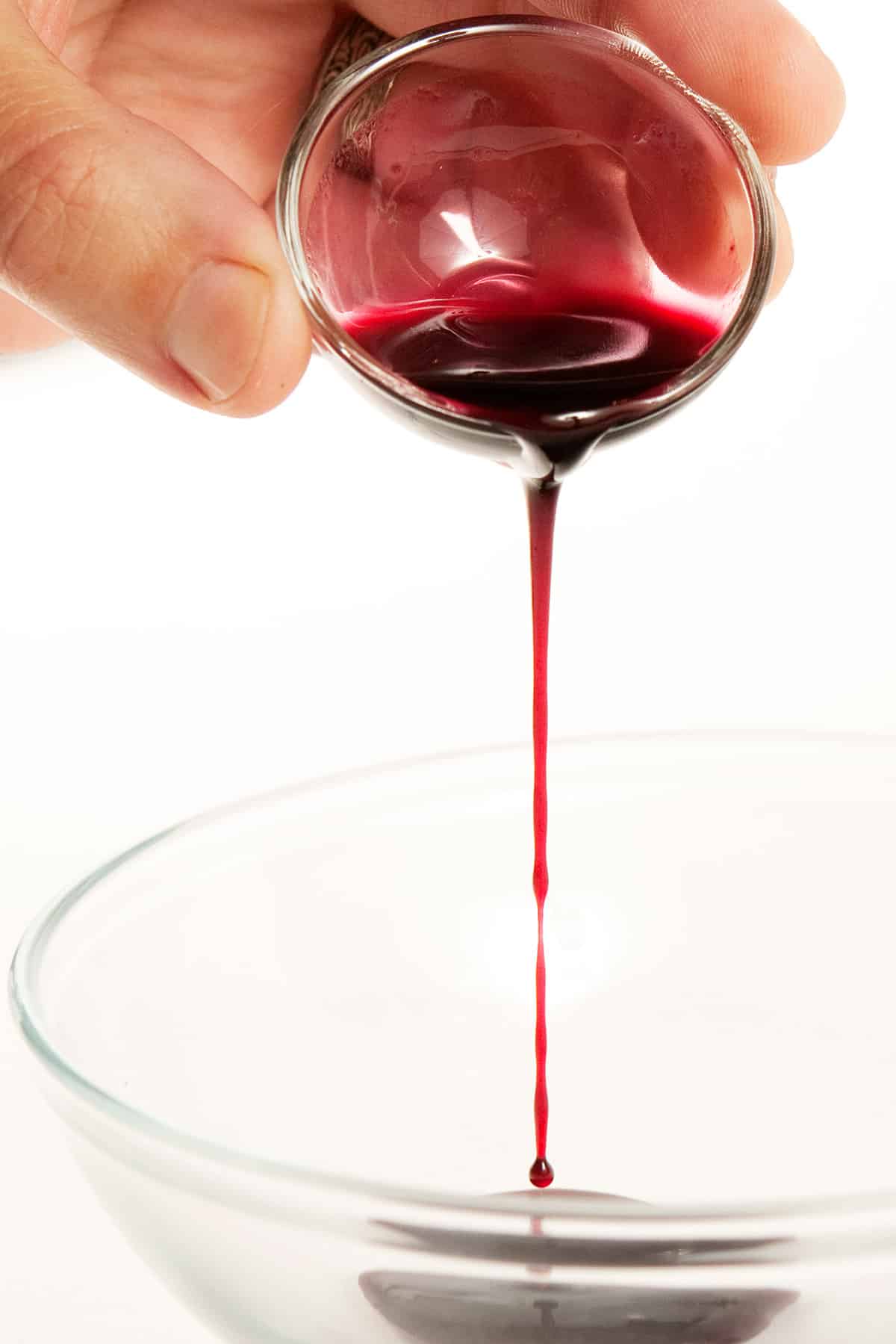 Pouring homemade elderberry syrup into a bowl.