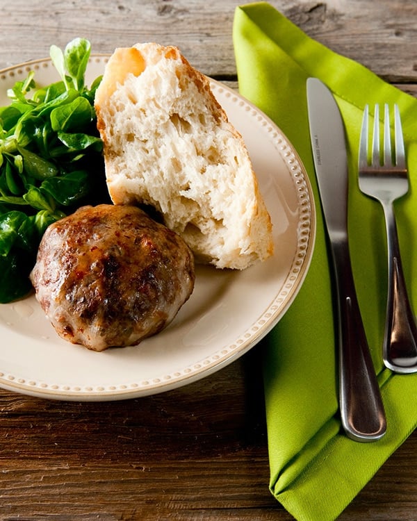 Cooked crepinettes on a plate with bread and a salad. 