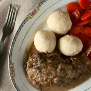 A plate of hasenpfeffer with semolina dumplings and glazed carrots.