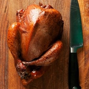 A whole smoked pheasant on a cutting board.