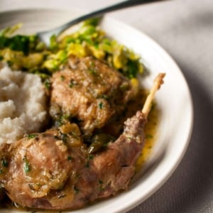 Italian rabbit, braised with mashed potatoes and greens, on a plate.