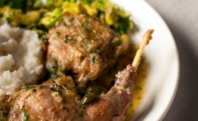 Italian rabbit, braised with mashed potatoes and greens, on a plate.
