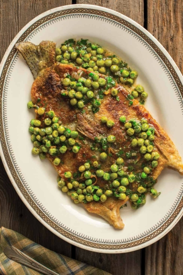 Butterflied trout with peas and parsley on a plate.
