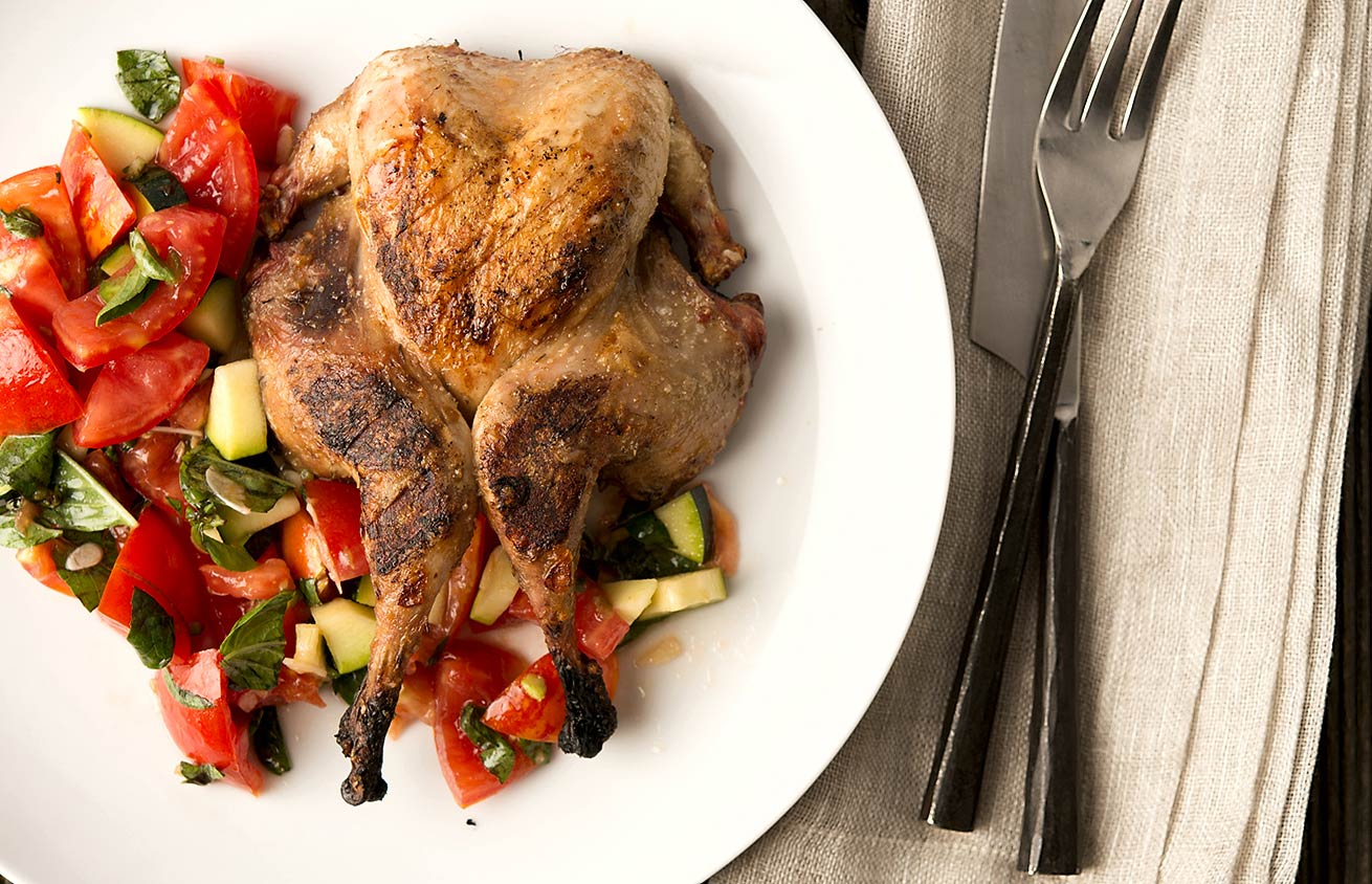 Grilled partridges with tomato salad on a plate. 