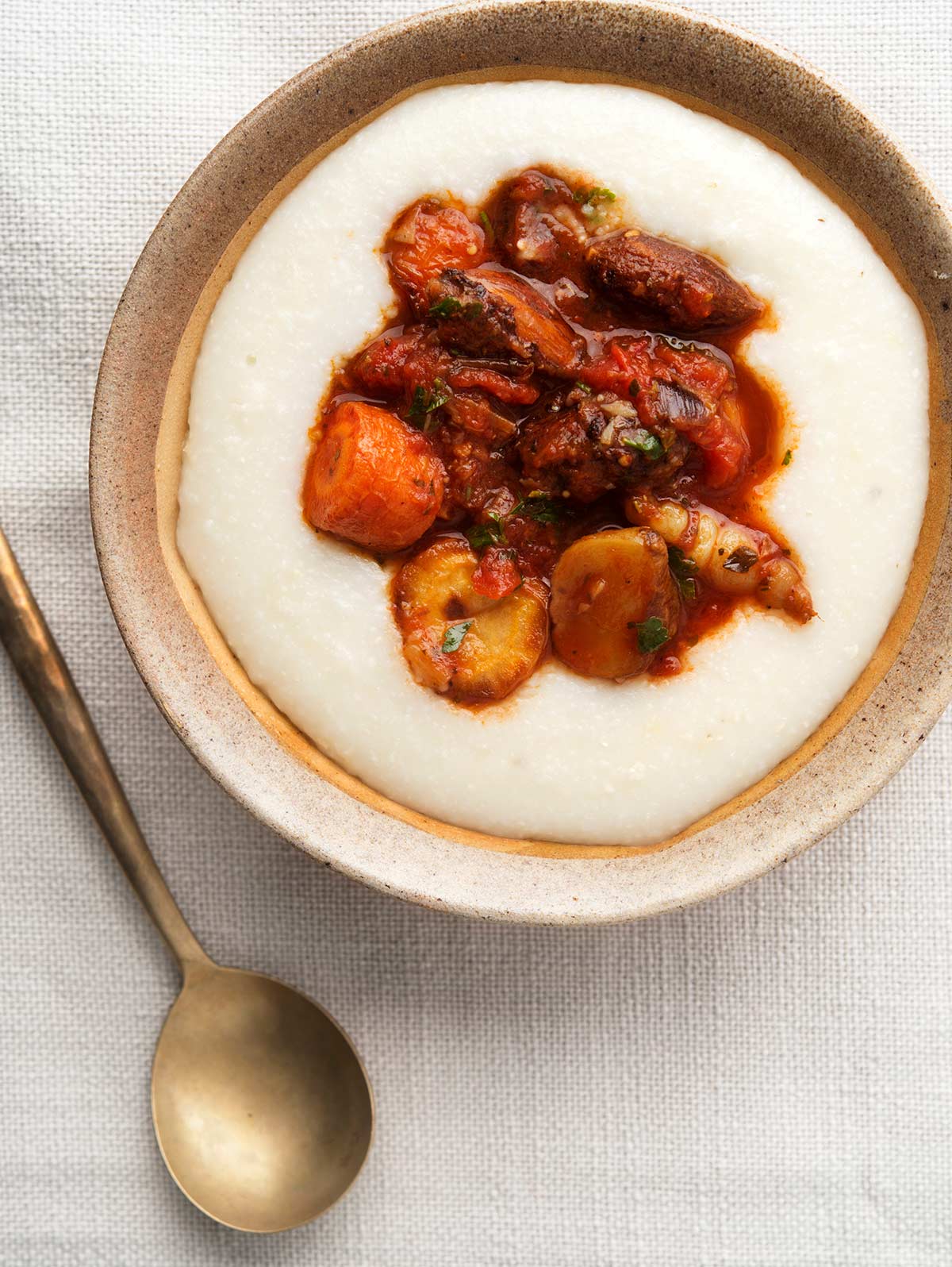 Root vegetable ragu in a bowl with polenta and a decorative spoon. 