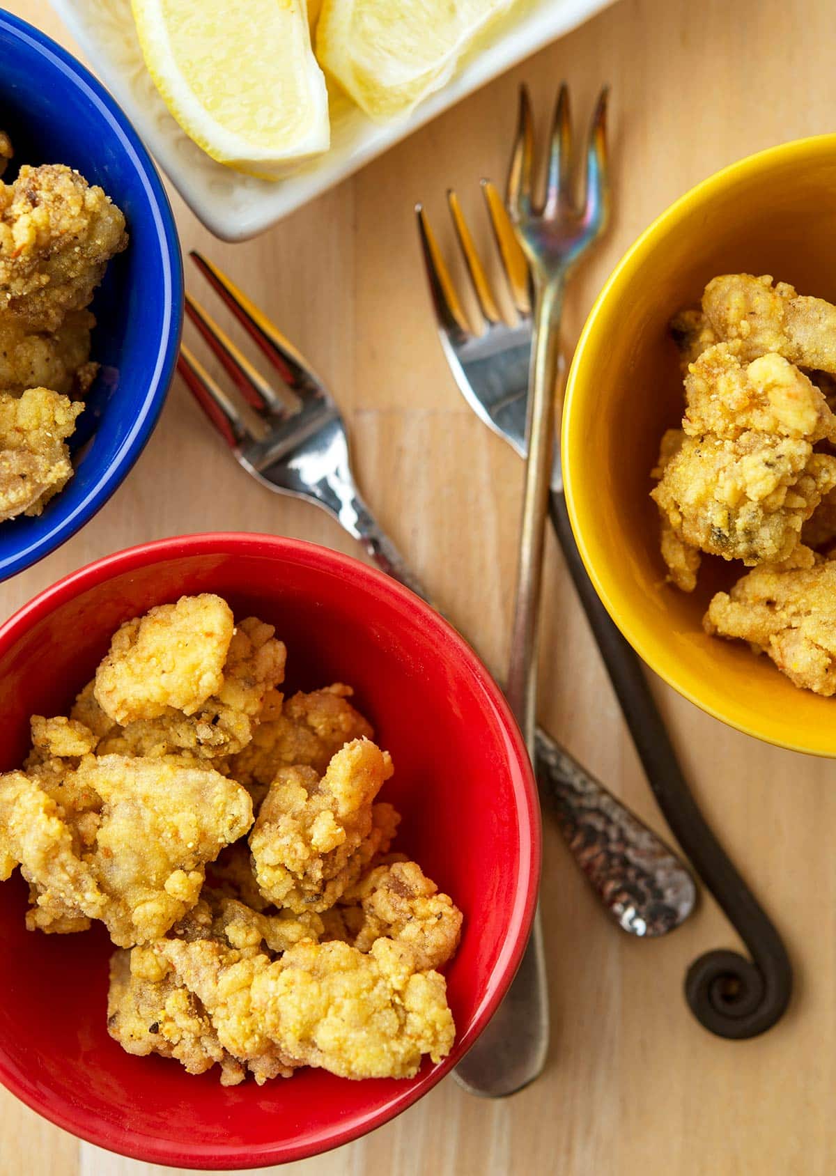 Fried clams in appetizer bowls with forks and lemon. 