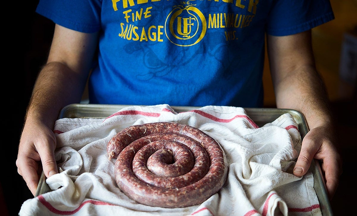 Holding a tray of boerewors sausages.