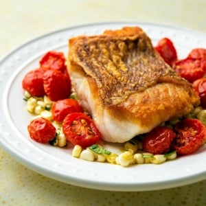 A plate of pan seared red snapper with cherry tomatoes.