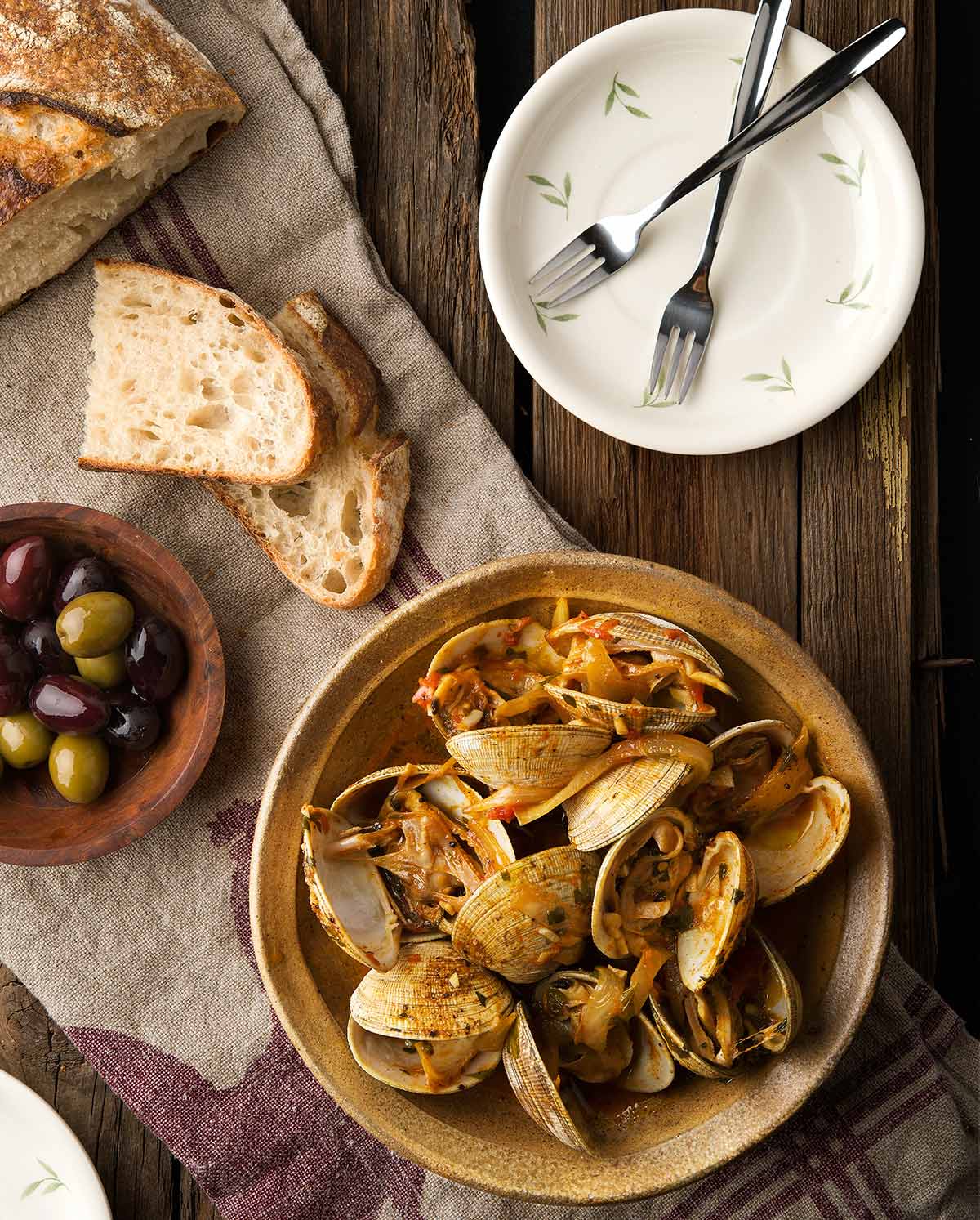 Overhead image of clams and chorizo with bread, olives and wine. 