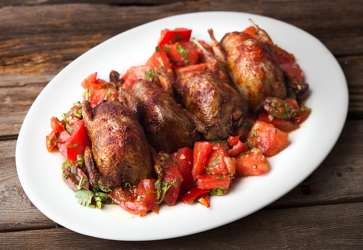 Four grilled doves on a platter with tomatoes. 