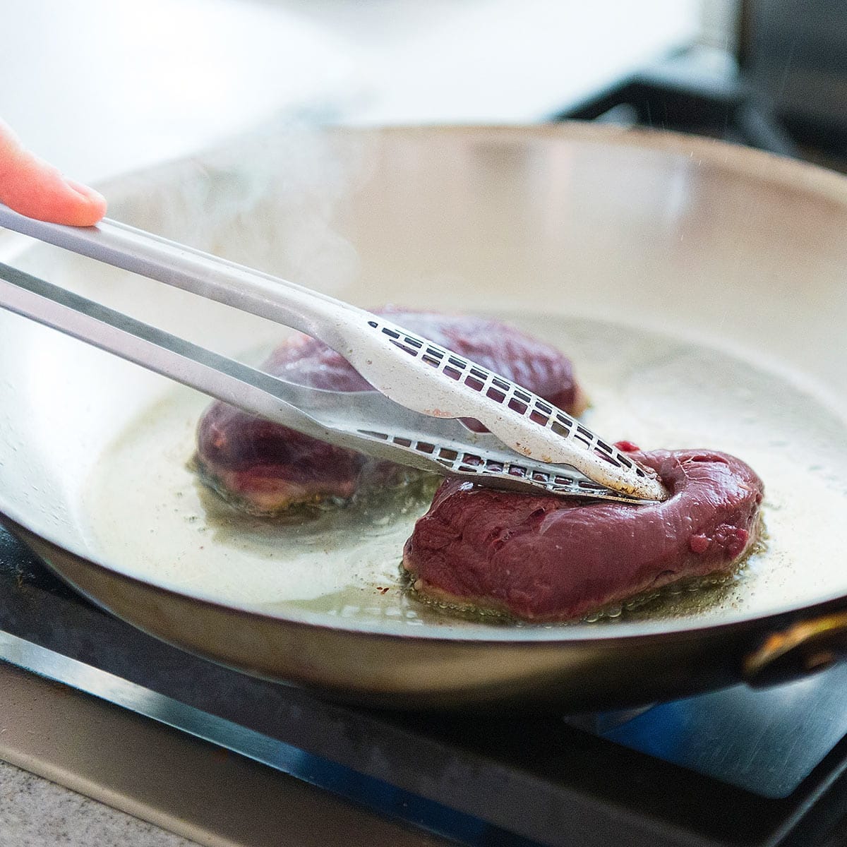 Pressing down a duck breast in a hot pan. 