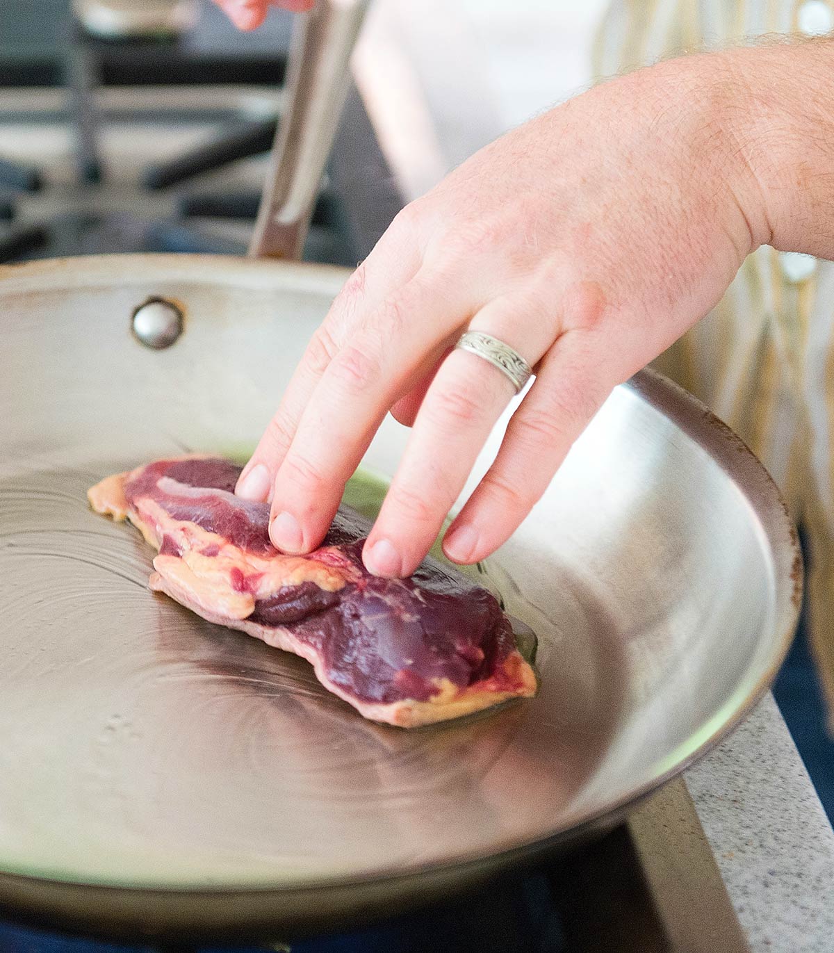 Spreading duck fat in a pan with a duck breast. 