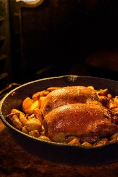 Slow roast duck in a cast iron pan with root vegetables.