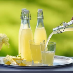 Pouring elderflower cordial into a glass, with bottles behind it.