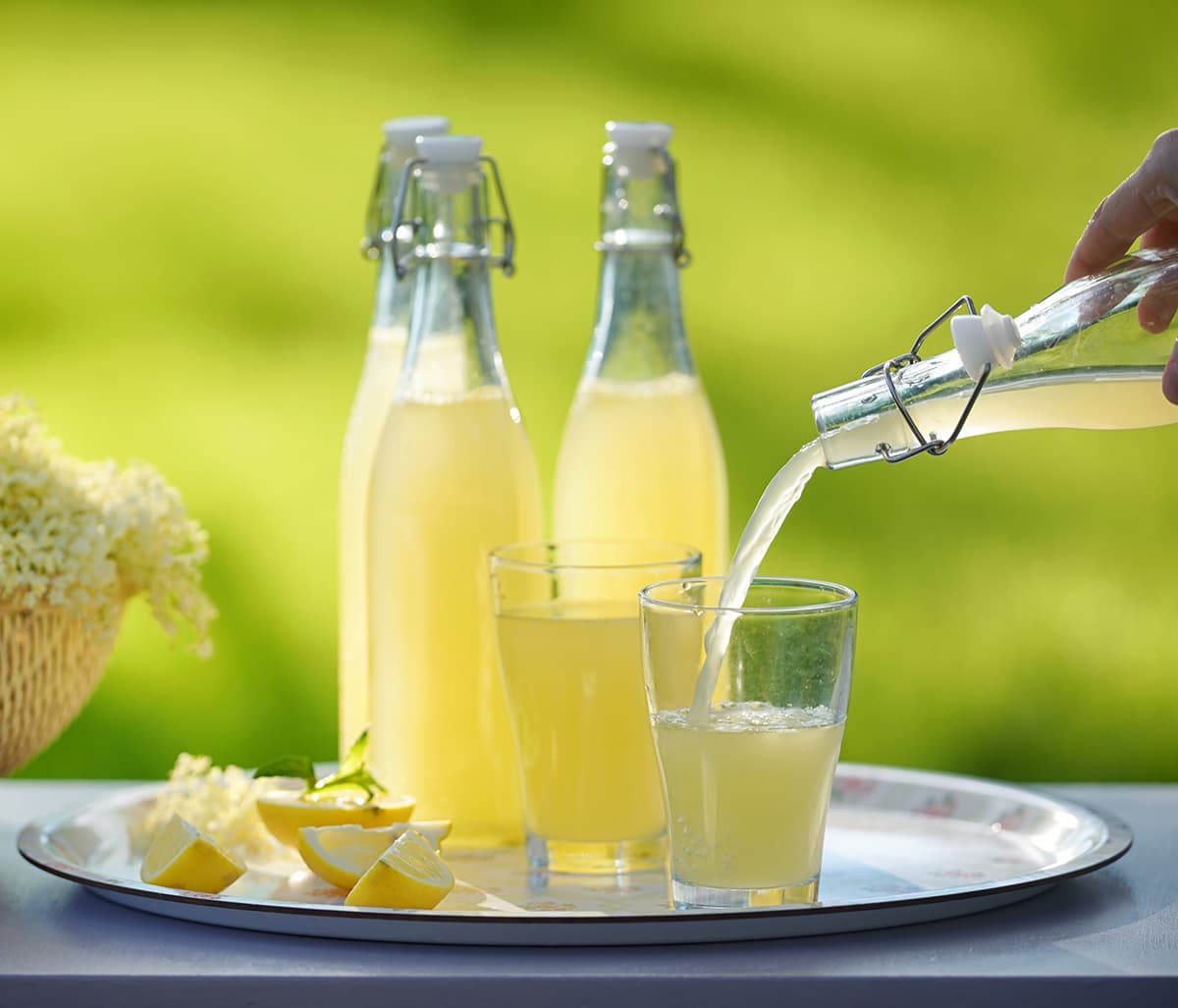 Pouring elderflower cordial into a glass, with bottles behind it. 