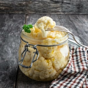 A jar of pickled cauliflower, with a fork removing one.