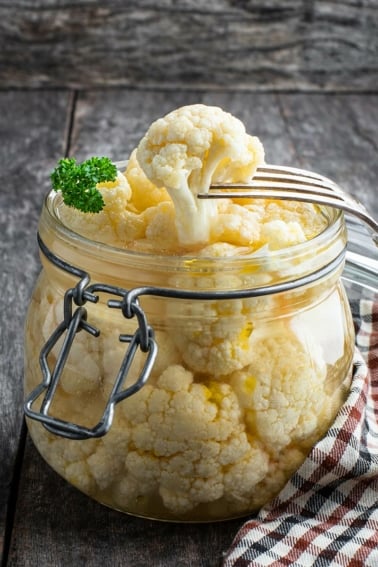 A jar of pickled cauliflower, with a fork removing one.