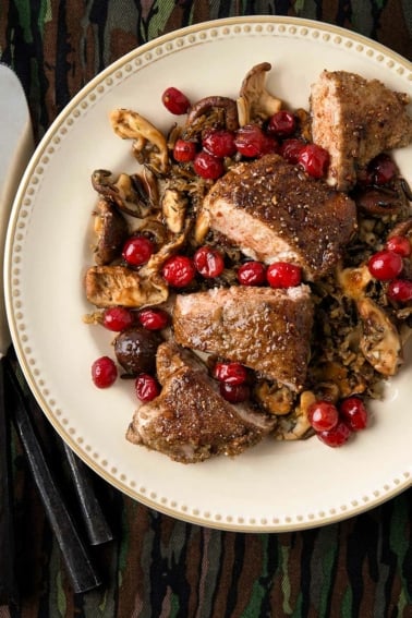 Grouse breast with mushrooms and cranberries on a plate.
