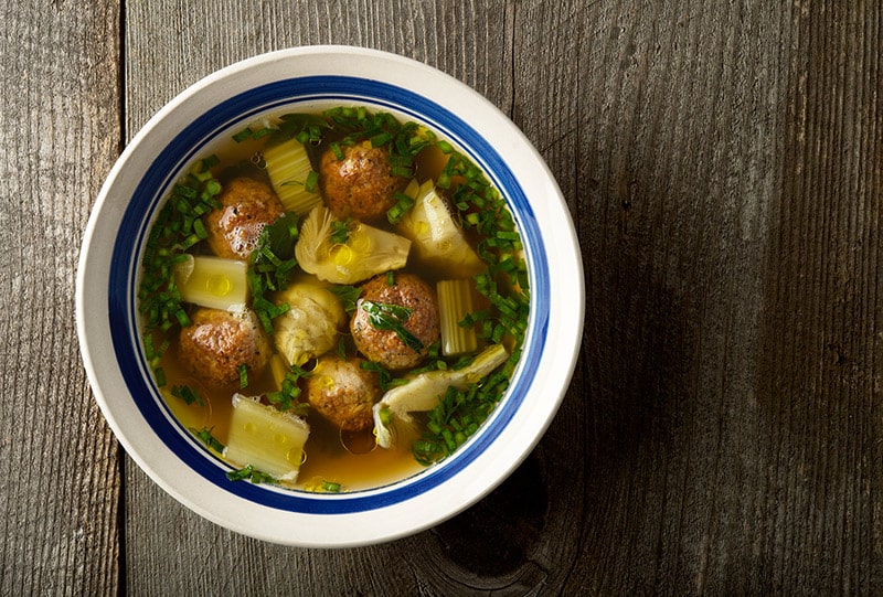 A bowl of artichoke soup with meatballs. 