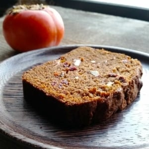 A slice of persimmon bread on a plate with a persimmon nearby