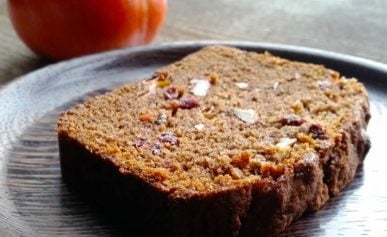 A slice of persimmon bread on a plate with a persimmon nearby