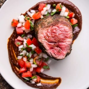 Elk tenderloin on a plate with ancho sauce and pico de gallo.