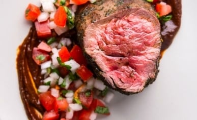 Elk tenderloin on a plate with ancho sauce and pico de gallo.