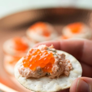 Hands holding salmon dip on a cracker with caviar.