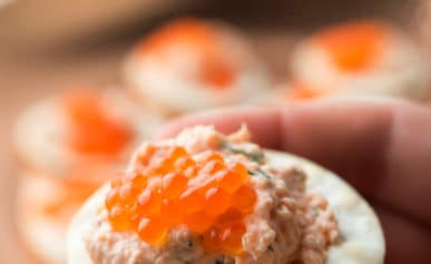 Hands holding salmon dip on a cracker with caviar.