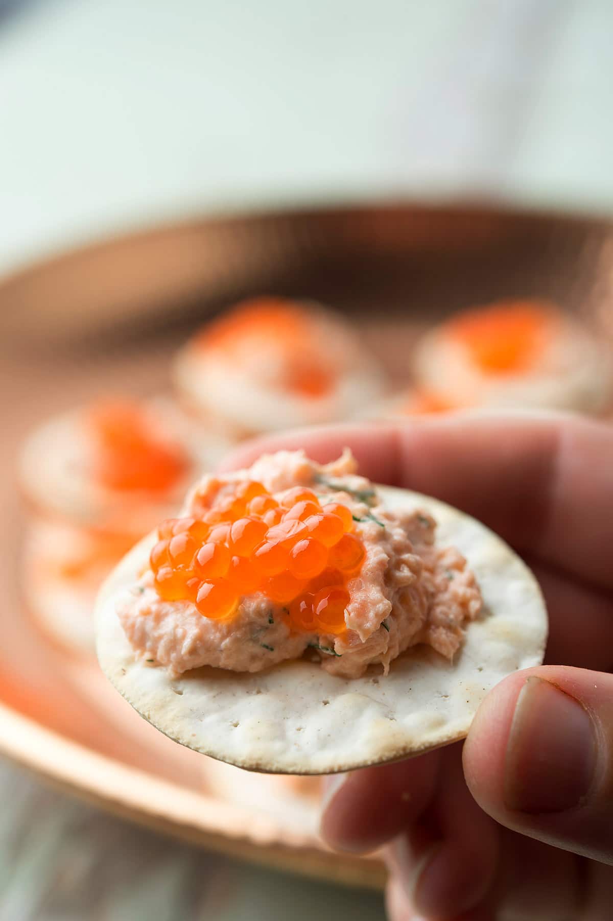 Hands holding salmon dip on a cracker with caviar