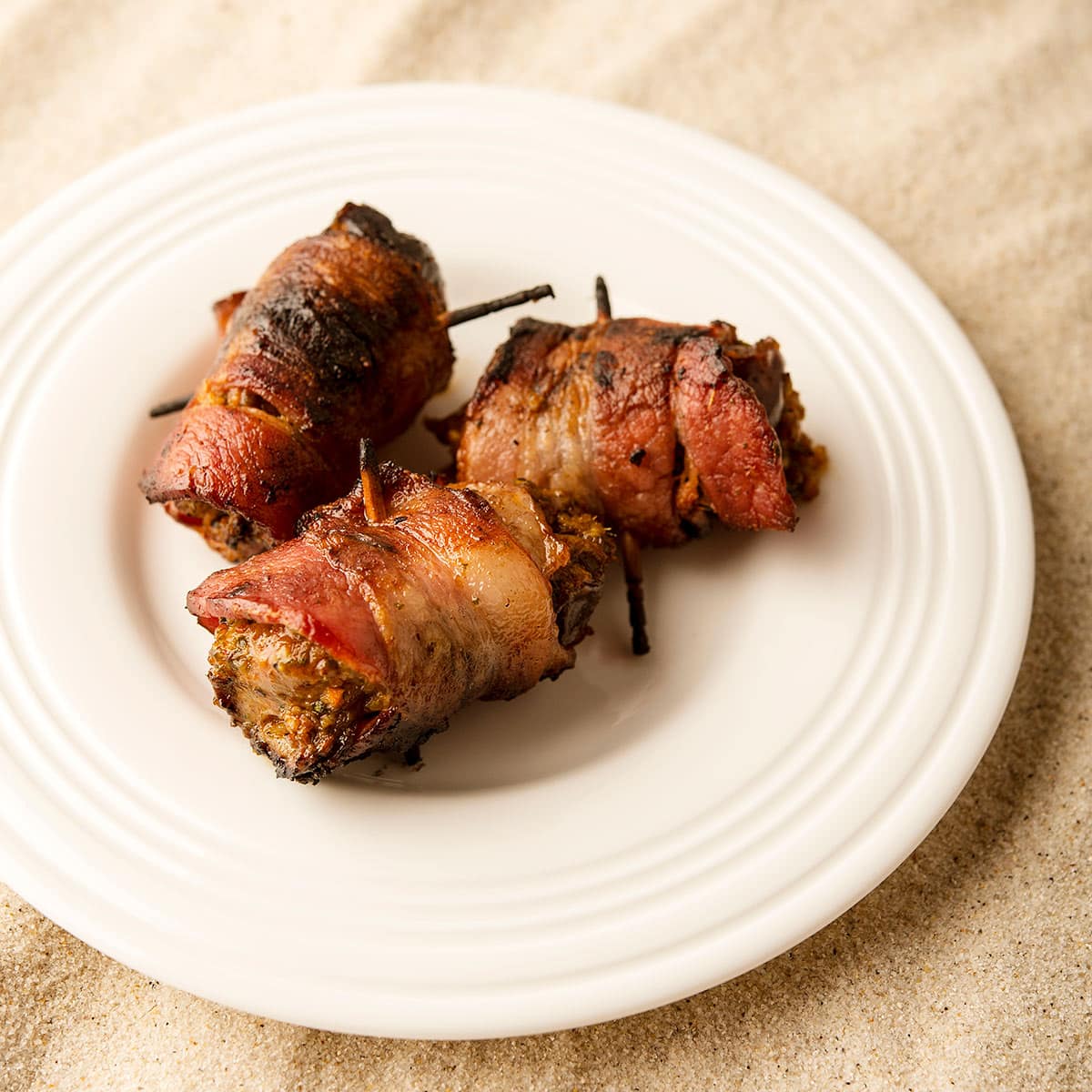 Three bacon wrapped dove breasts on a plate. 