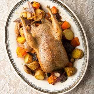 A roast prairie chicken over a bed of roasted root vegetables.