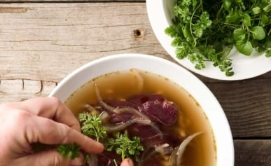 Adding herbs to a bowl of goose soup.