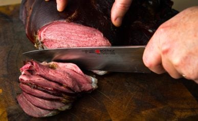 Slicing smoked venison on a cutting board.