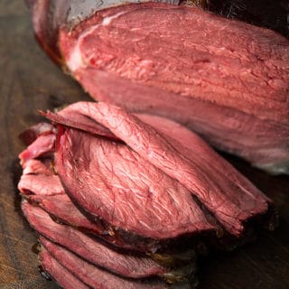 A smoked venison leg, sliced on a cutting board.