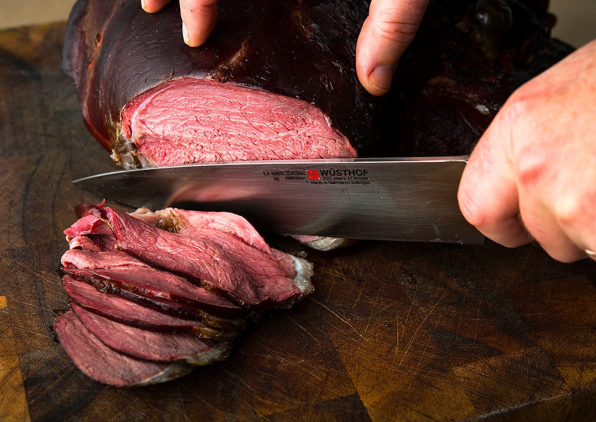Slicing a smoked venison roast on a cutting board. 