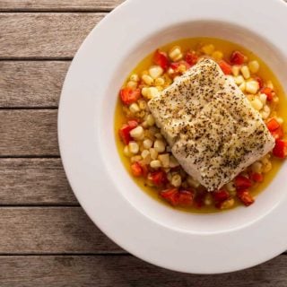 Butter poached tripletail over corn and peppers, in a shallow bowl.
