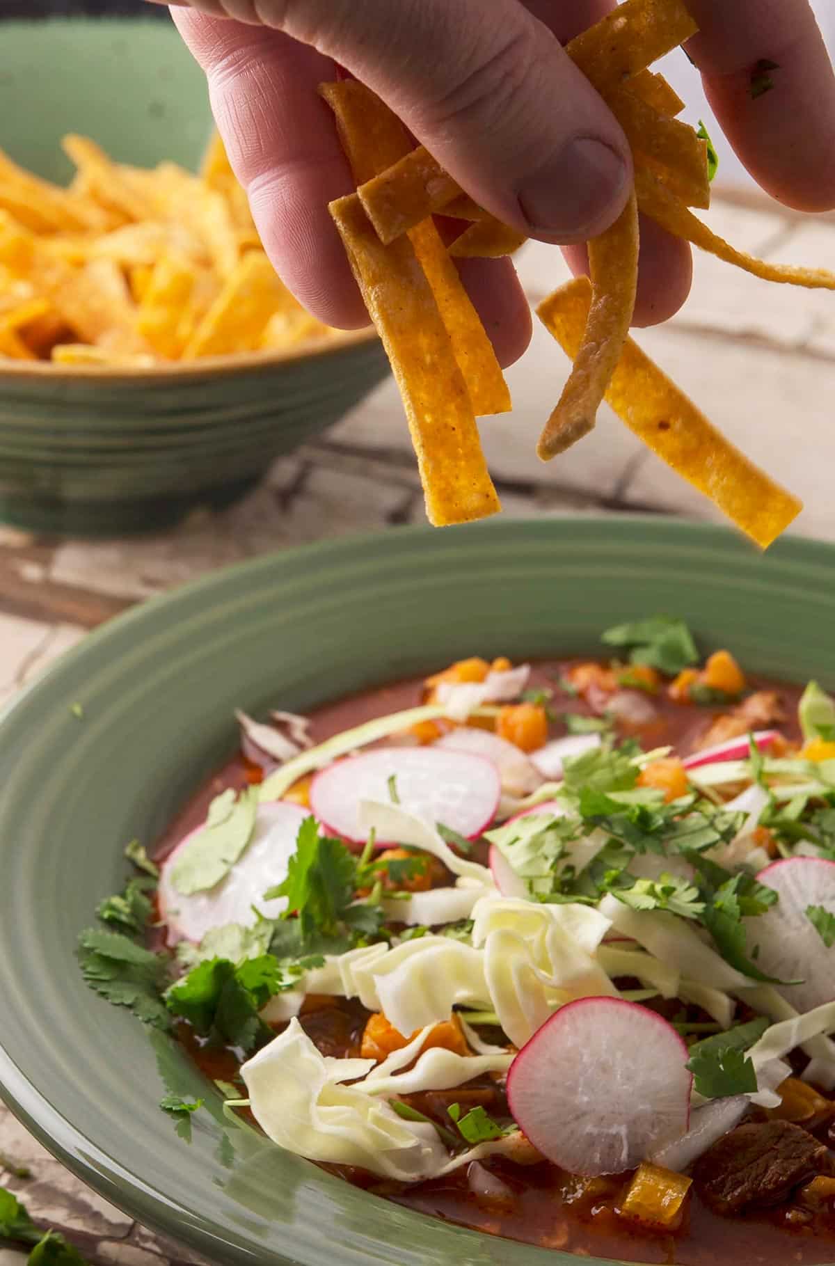 Adding totopos to a bowl of pozole rojo