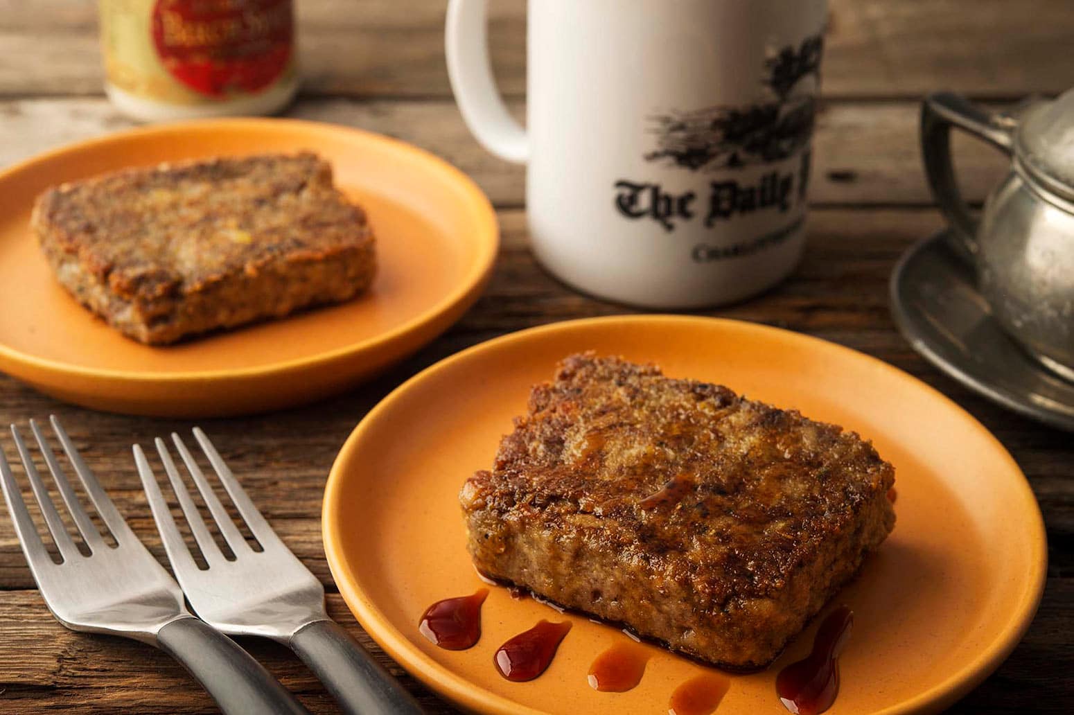 Two plates of scrapple with a cup of coffee. 