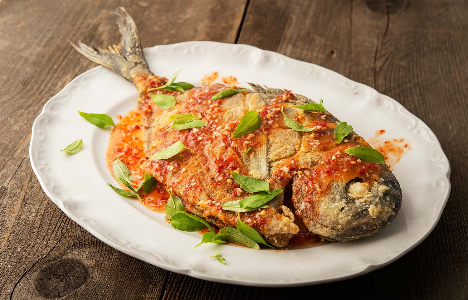 Thai fried pomfret fish with chile sauce on a platter. 