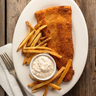 fried flounder with tartar sauce and homemade fries on the plate.